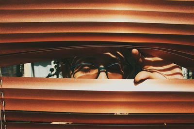 Close-up of person seen through blinds on sunny day