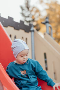 Cute little boy with down syndrome in hat walks in the playground, rolling down the children's slide