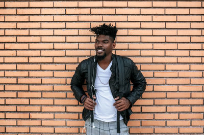 Portrait of young man standing against brick wall