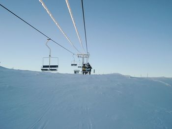 People traveling on ski lift over snow covered landscape against clear sky