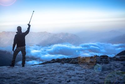 Rear view of man standing on mountain against sky