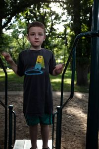 Portrait of boy standing by railing at park