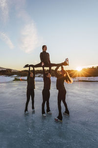 Female figure skaters practicing on frozen lake at sunset