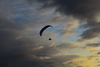 Low angle view of person paragliding against cloudy sky at sunset