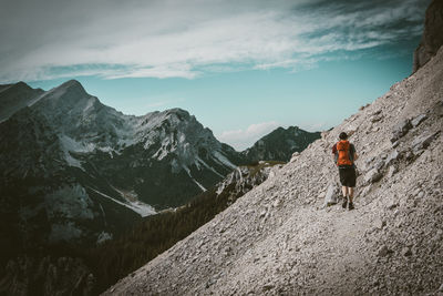 Rear view of man walking on mountain against sky