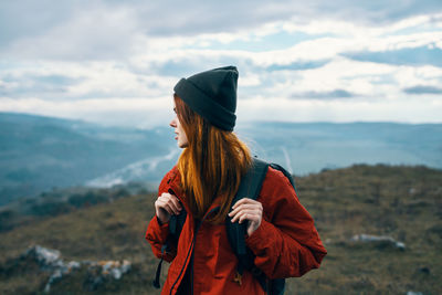 Young woman standing on rock against sky