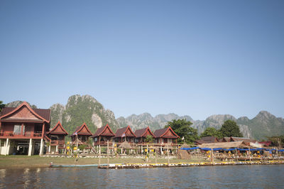 Houses by lake against clear blue sky