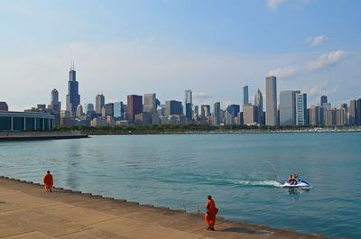 People on sea by cityscape against sky