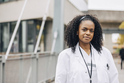 Portrait of confident female doctor in lab coat outside hospital