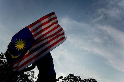 Low angle view of man with malaysian flag standing against sky