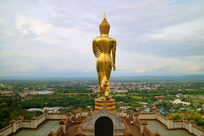 Gold colored buddha image in walking posture facing the town of nan, thailand