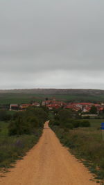 Road passing through field against cloudy sky