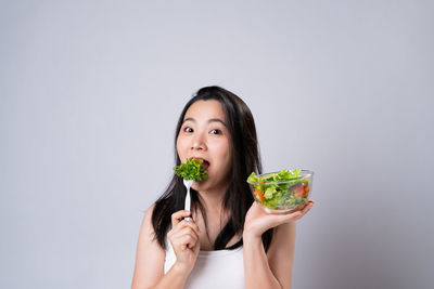 Portrait of young woman holding ice cream against white background