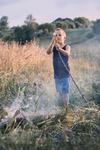 Boy holding marshmallow with stick while standing on field