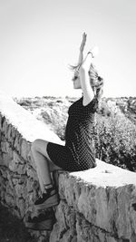 Portrait of woman with arms raised on beach against clear sky