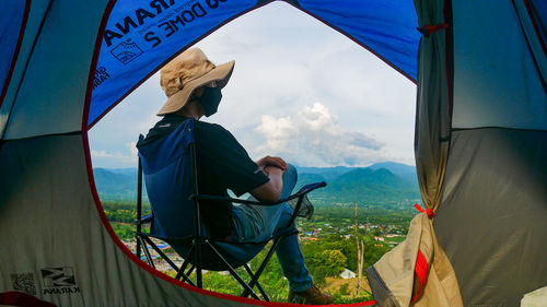Rear view of man sitting on tent against sky