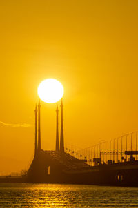 Silhouette bridge over sea against orange sky