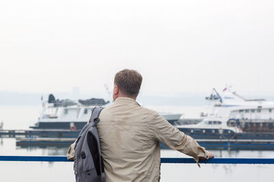 Man with a backpack in a wet jacket is waiting for his ship in the rain.