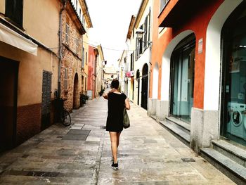 Full length rear view of woman walking on footpath amidst buildings in city