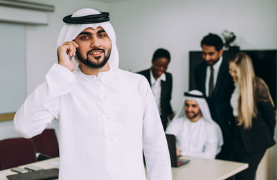 Smiling businessman talking on mobile phone against colleagues in meeting at office