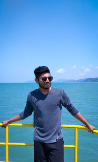 Young man wearing sunglasses standing against sea