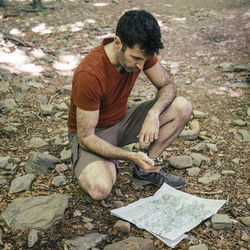 Man reading map while crouching in forest