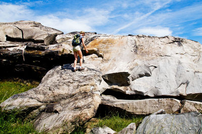 Female hiker standing on rock formation against sky during sunny day