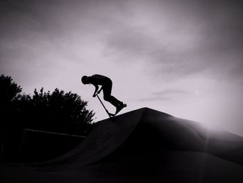 Silhouette man riding scooter against sky