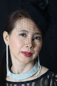 Close-up portrait of woman wearing lipstick and jewelry against black background