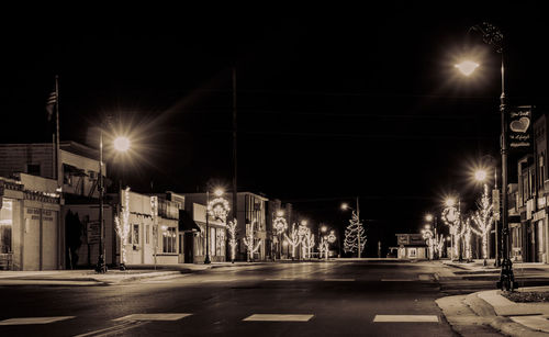 Illuminated street amidst buildings against sky at night