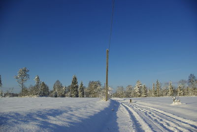 Pole by tire tracks on snow covered field against clear blue sky