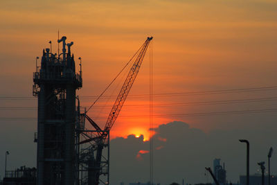 Silhouette cranes at construction site during sunset