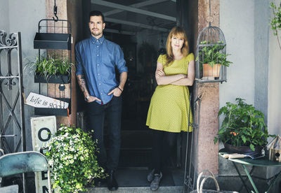 Portrait of confident female owner with colleague leaning at store doorway