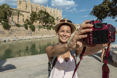 Close-up of young woman taking picture by lake against built structure