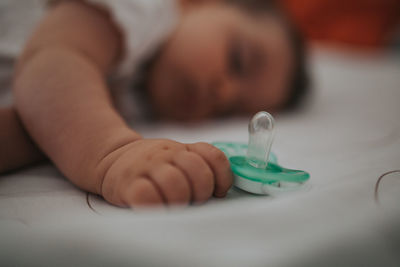 Close-up of cute baby girl holding pacifier while sleeping on bed