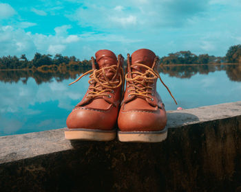 Low section of person wearing shoes by swimming pool against lake