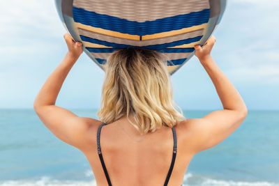 Rear view of woman holding surfboard overhead at beach
