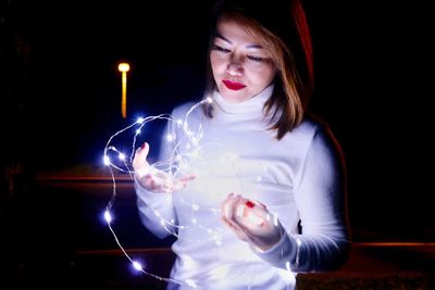 Young woman touching illuminated lighting equipment against black background