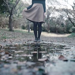 Low section of woman standing in front of puddle at forest