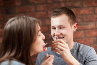 Boyfriend feeding girlfriend against brick wall