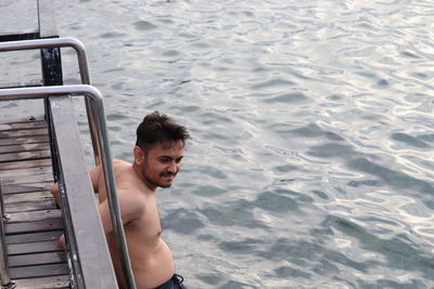 A shirtless young man standing on dock by sea water