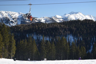 Low angle view of people sitting in ski lift against snowcapped mountains during winter