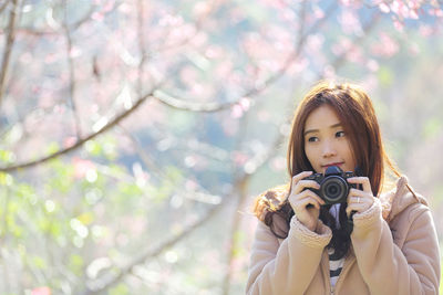 Portrait of young woman photographing against trees