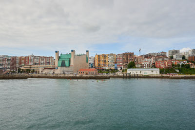 Buildings by river against cloudy sky