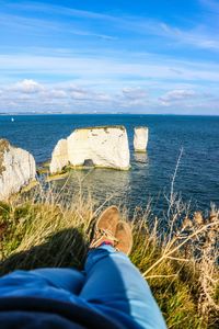 Low section of man relaxing on beach against sky