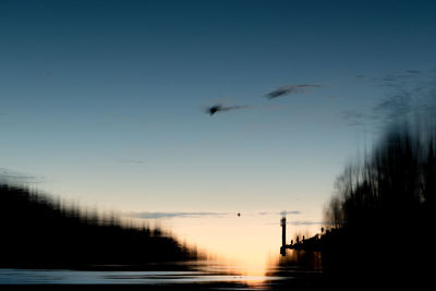 Silhouette bird flying over lake against sky during sunset