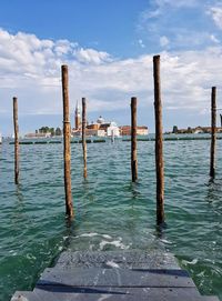 Wooden posts in sea against sky