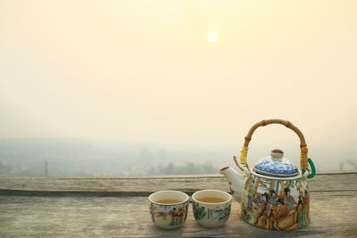 Teapot with tea cups on table against sky during morning