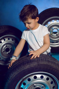 Boy in a white t shirt shirt and hat sits on a background of car wheels on a blue