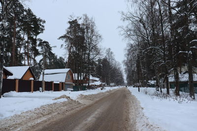 Snow covered road amidst trees against sky